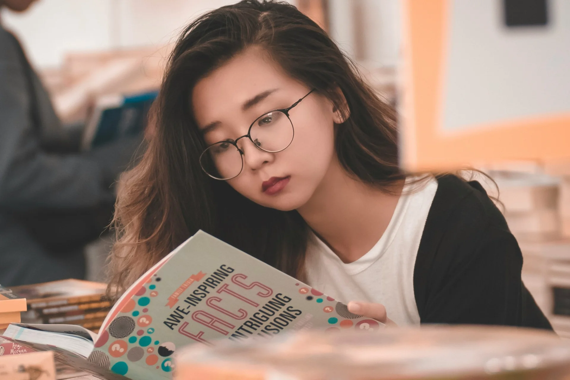 A student in glasses reading a textbook at a desk