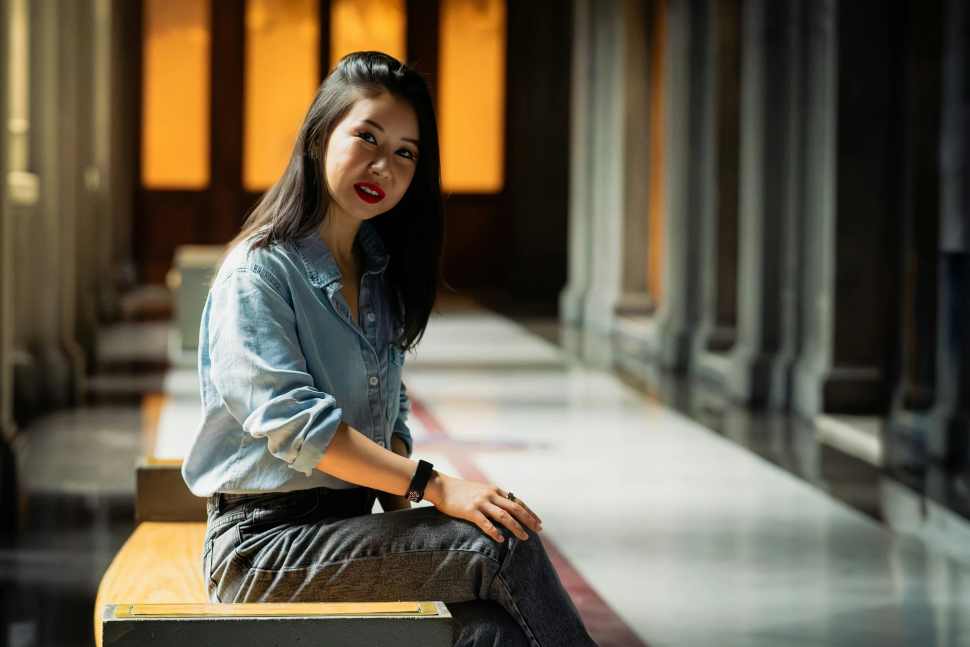 Young woman in a denim shirt sitting on a bench in a long hallway
