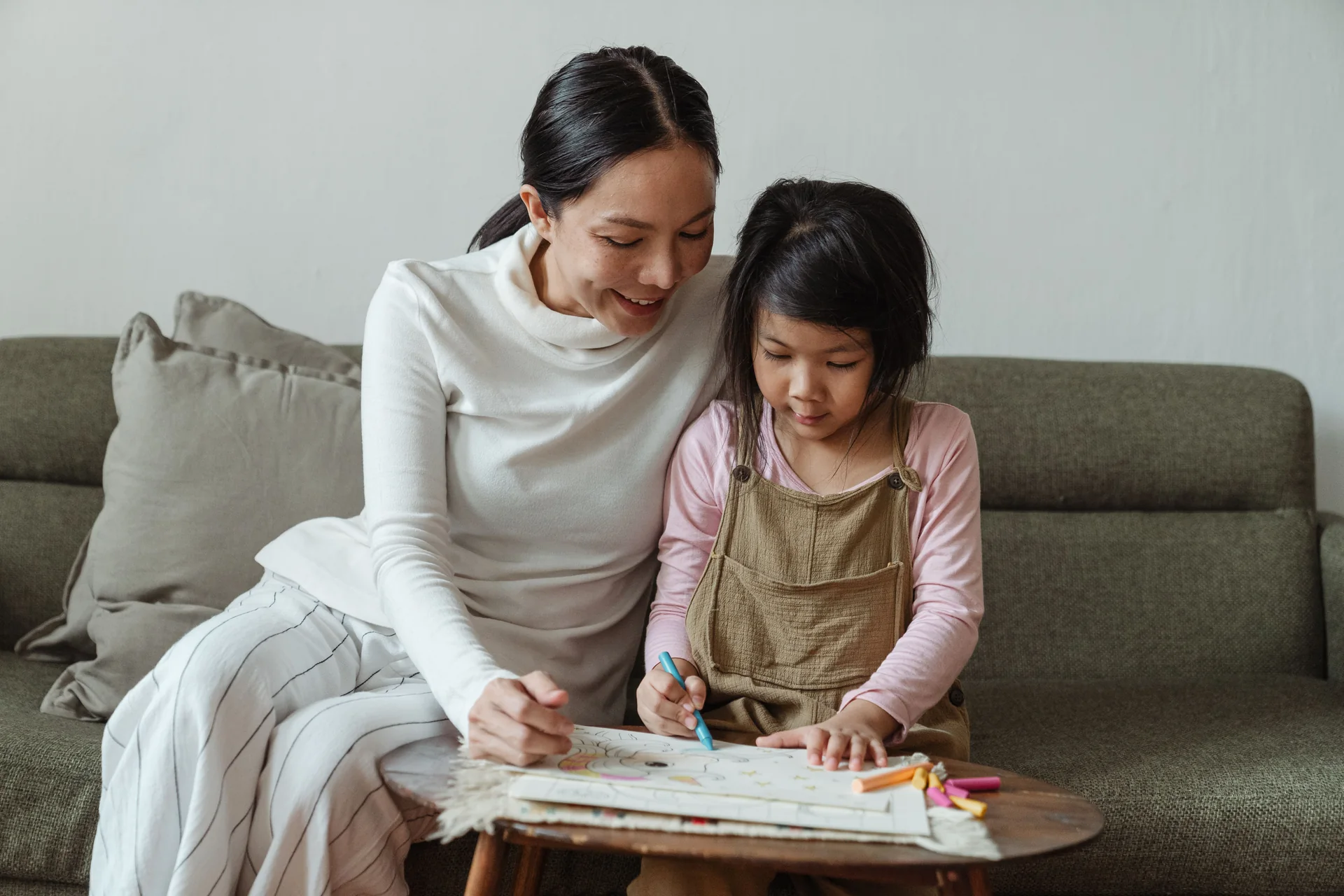 A woman helping a young girl with a colouring activity at home